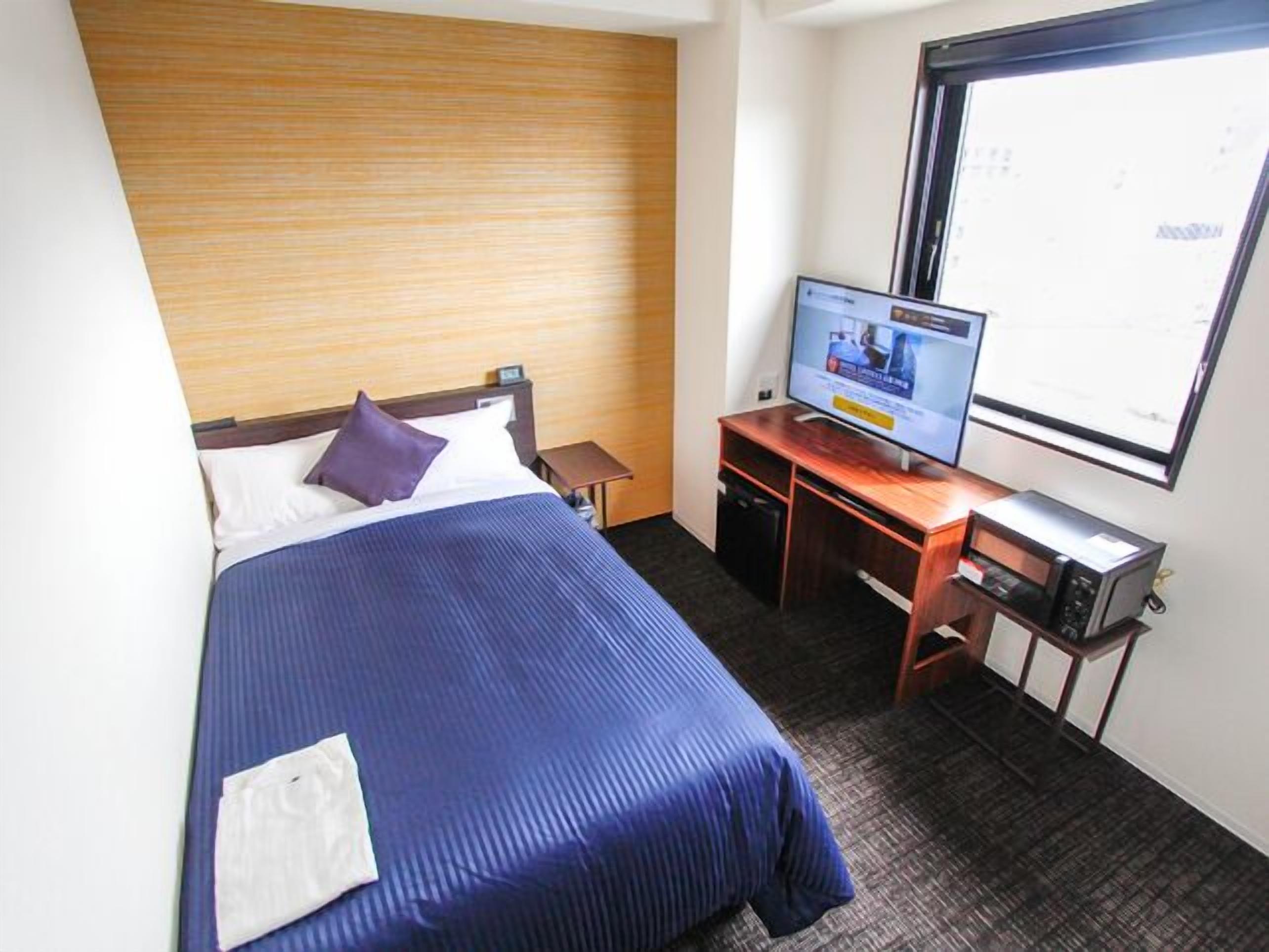 Ein Hotelzimmer mit Bett, Fernseher, Schreibtisch und Fenster.