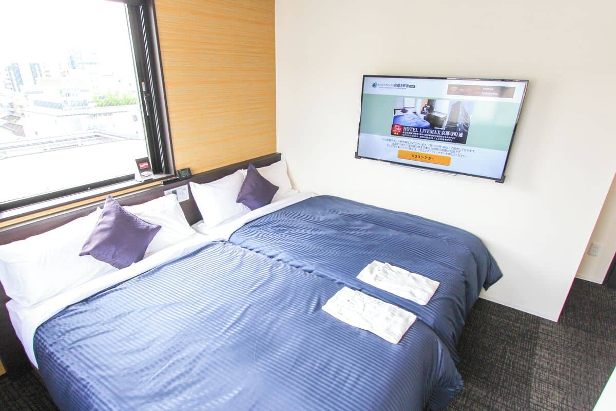 Habitación de hotel con dos camas, un televisor en la pared y una ventana con persianas.