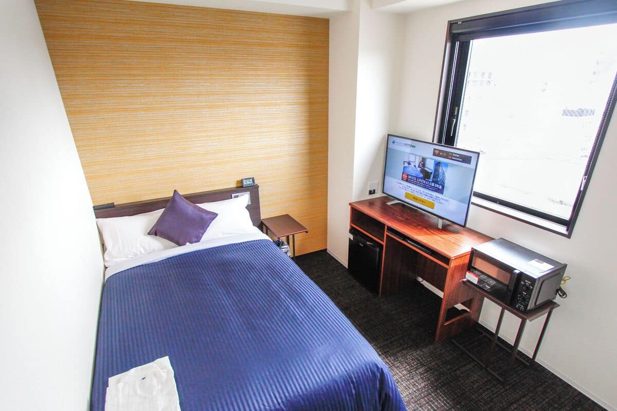 Una habitación de hotel con una cama, un escritorio con ordenador y una ventana.