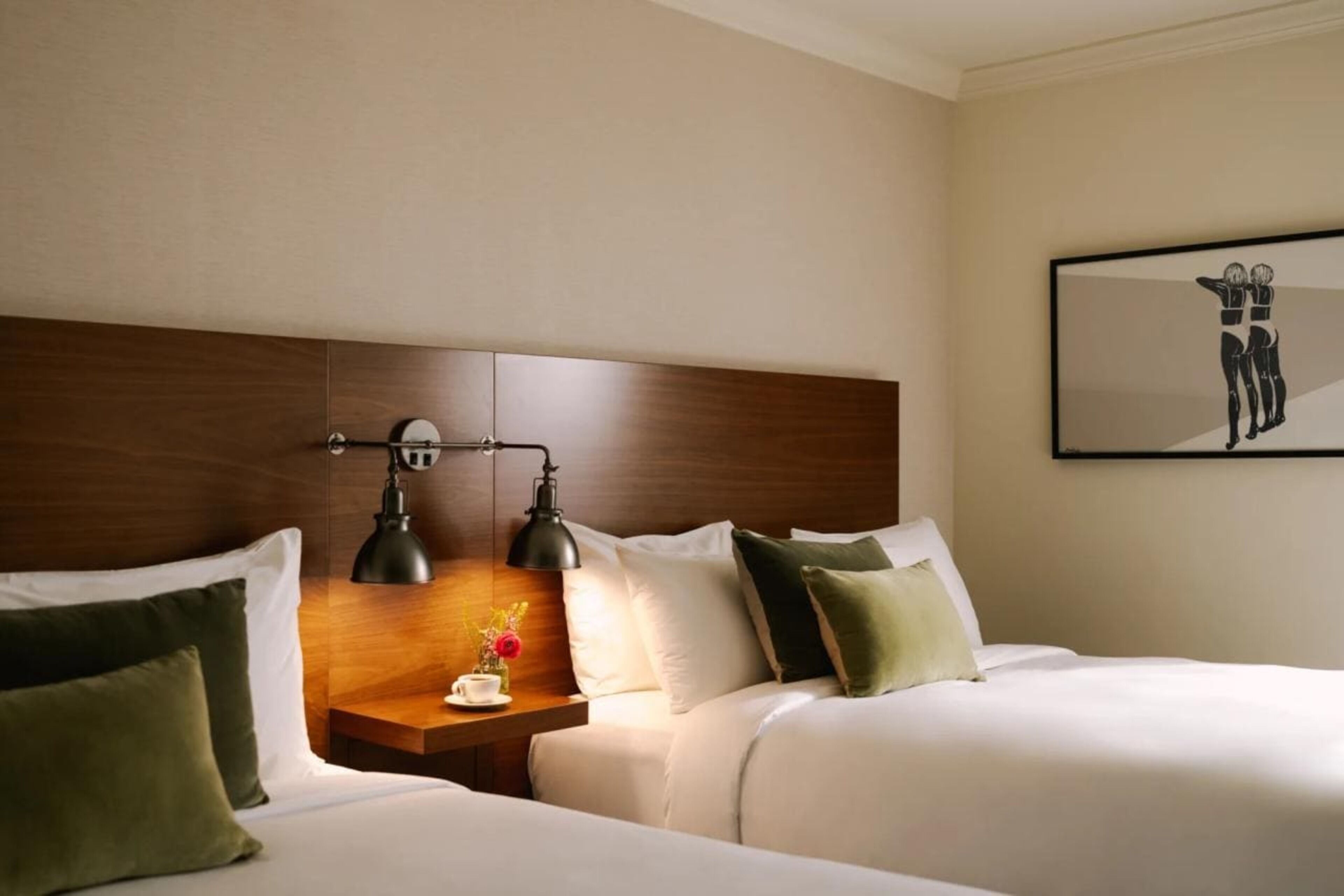 A hotel room with two beds, a wooden headboard, bedside tables with lamps, and a framed artwork on the wall.