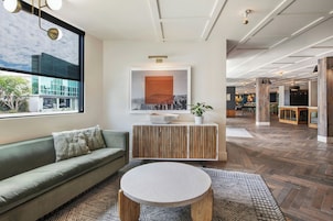 A modern hotel lobby with a green sofa, a round table, and a large window offering a view of the outside.