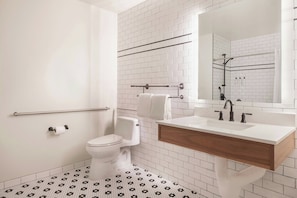 A bathroom with white subway tiles, a white toilet, a wooden vanity with a sink, and a mirror. - FOUND Hotels, Santa Monica, Series by Marriott (Los Angeles)