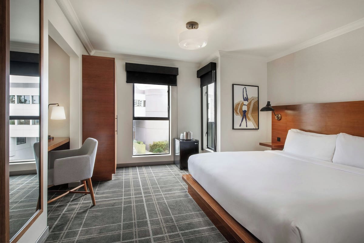 Habitación de hotel con una cama grande, un escritorio con silla, una mesita, una ventana con vistas y una lámpara en el techo.