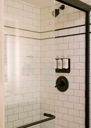 A shower area with white tiled walls, a glass door, and a black showerhead. - FOUND Hotels, Santa Monica, Series by Marriott (Los Angeles)