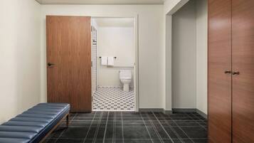 A hallway with a bench, a wooden door, and a view into a bathroom with a toilet and a towel rack.