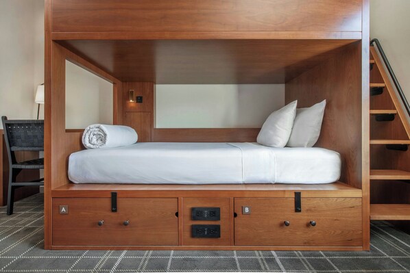 Un lit compact en bois, doté d’un matelas, de coussins et d’un petit meuble de rangement à deux compartiments, étiquetés A et B.