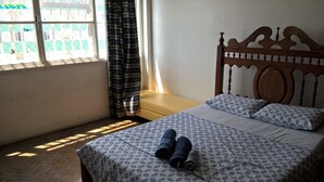 A bedroom with a bed, a window with curtains, and a view of a building outside. - Maria Izabel (Salvador)