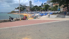 Paseo marítimo frente a la playa, con un camino empedrado, sombrillas y algunas personas.