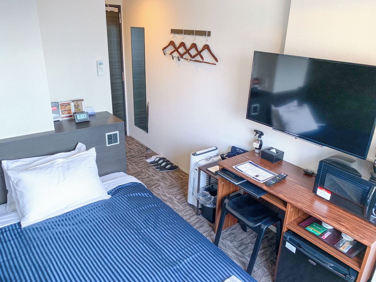 A hotel room with a bed, desk, television, and a wall-mounted coat rack.