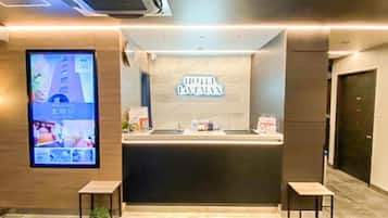 A hotel reception area with a modern design, featuring a reception desk, a digital screen displaying hotel information, and a sign above the desk.
