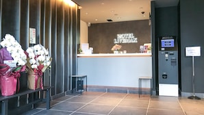 A hotel reception area with a modern design, featuring a reception desk, a digital check-in kiosk, and a bench with flower arrangements. - Hotel Livemax Chiba Sogaekimae (Chiba)