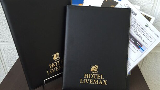 Two black binders with 'HOTEL LIVEMAX' branding and a logo, placed on a table with some papers.