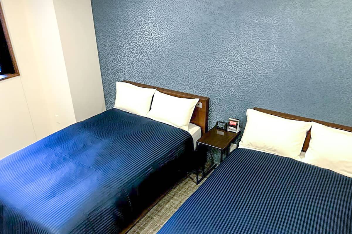 Habitación de hotel con dos camas, una mesita y una mesilla de noche.