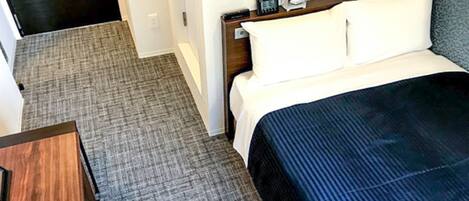 Una habitación de hotel con una cama, una mesita de noche, un reloj digital y un termostato.