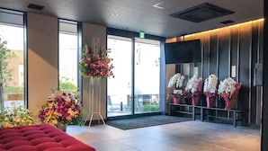 A hotel lobby with a red cushioned seating area, a tall floral arrangement, and a row of white flowers on a stand. - Hotel Livemax Chiba Sogaekimae (Chiba)
