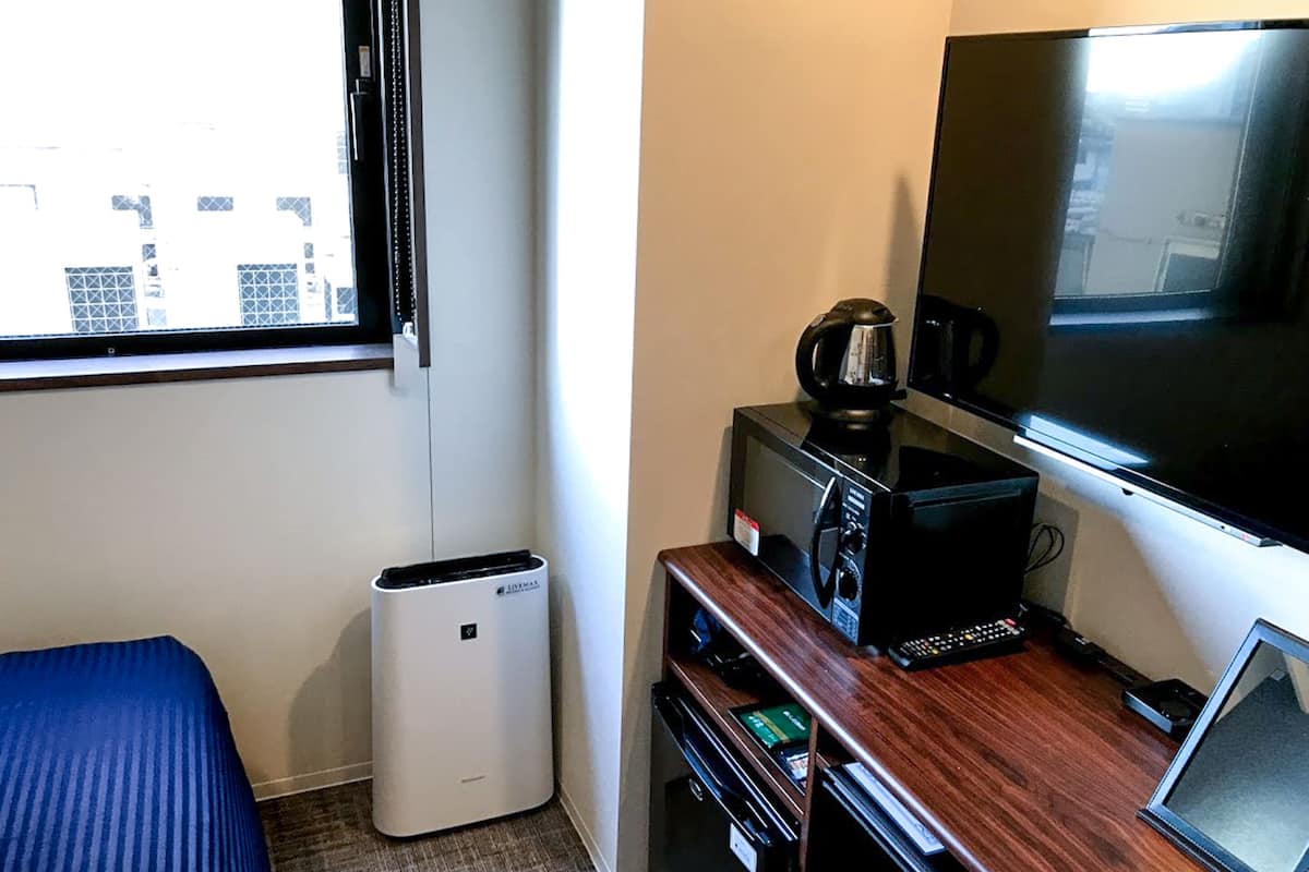 Una habitación de hotel con cama, escritorio con cafetera, televisión y cubo de basura.