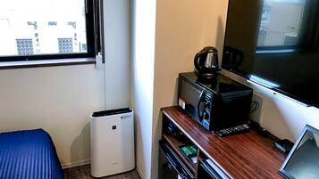 A hotel room with a bed, a desk with a coffee maker, a TV, and a trash bin.