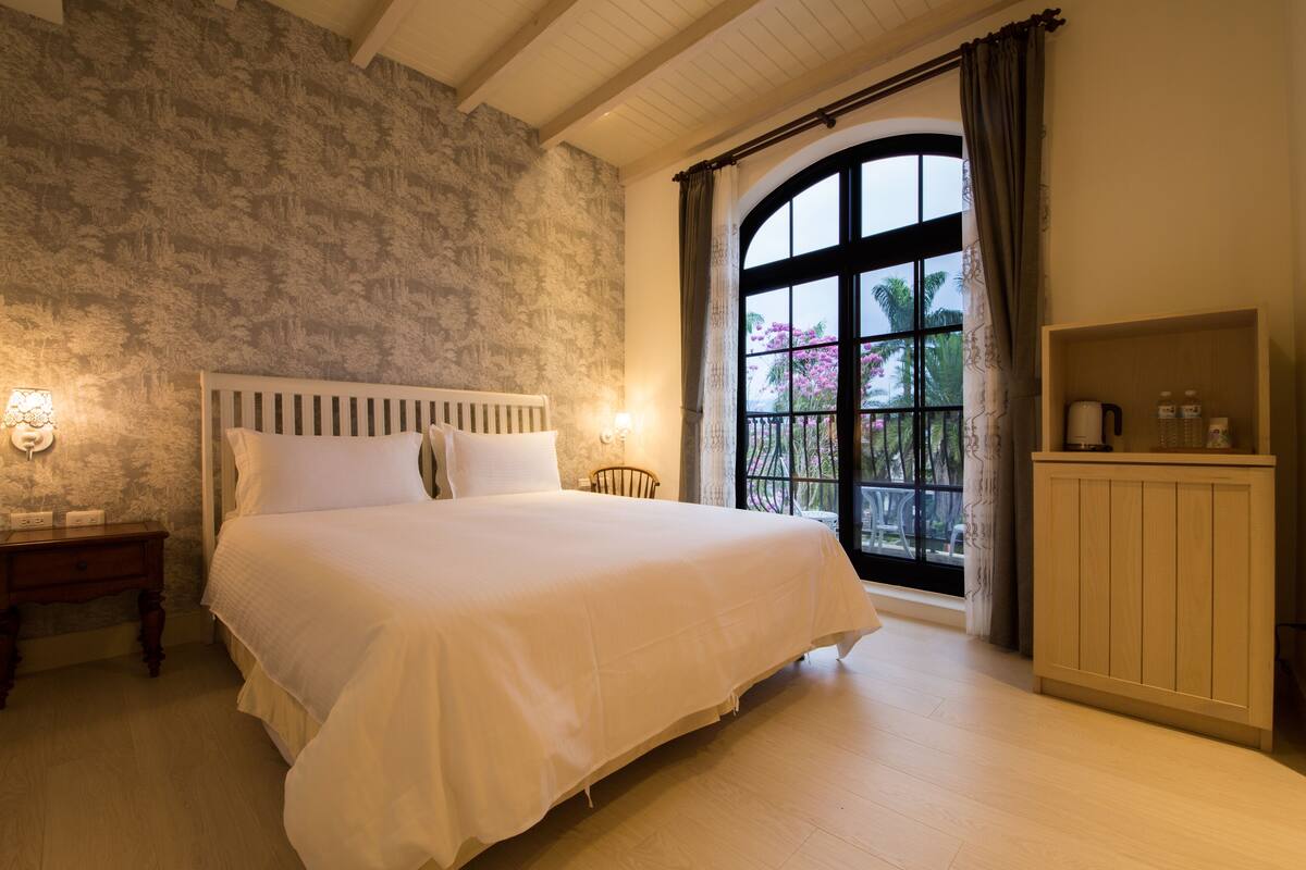 A bedroom with a large bed, a nightstand, a wooden cabinet, and a window with curtains.