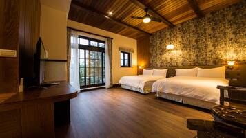 A hotel room with a wooden ceiling, two beds, a desk, and a large window with curtains.