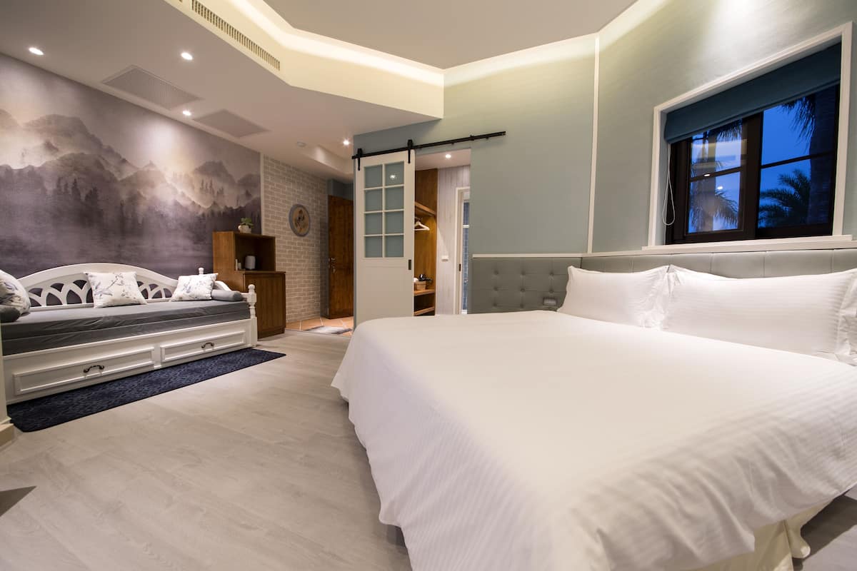 A bedroom with a large bed, a bench, a mural, and a window with a view.