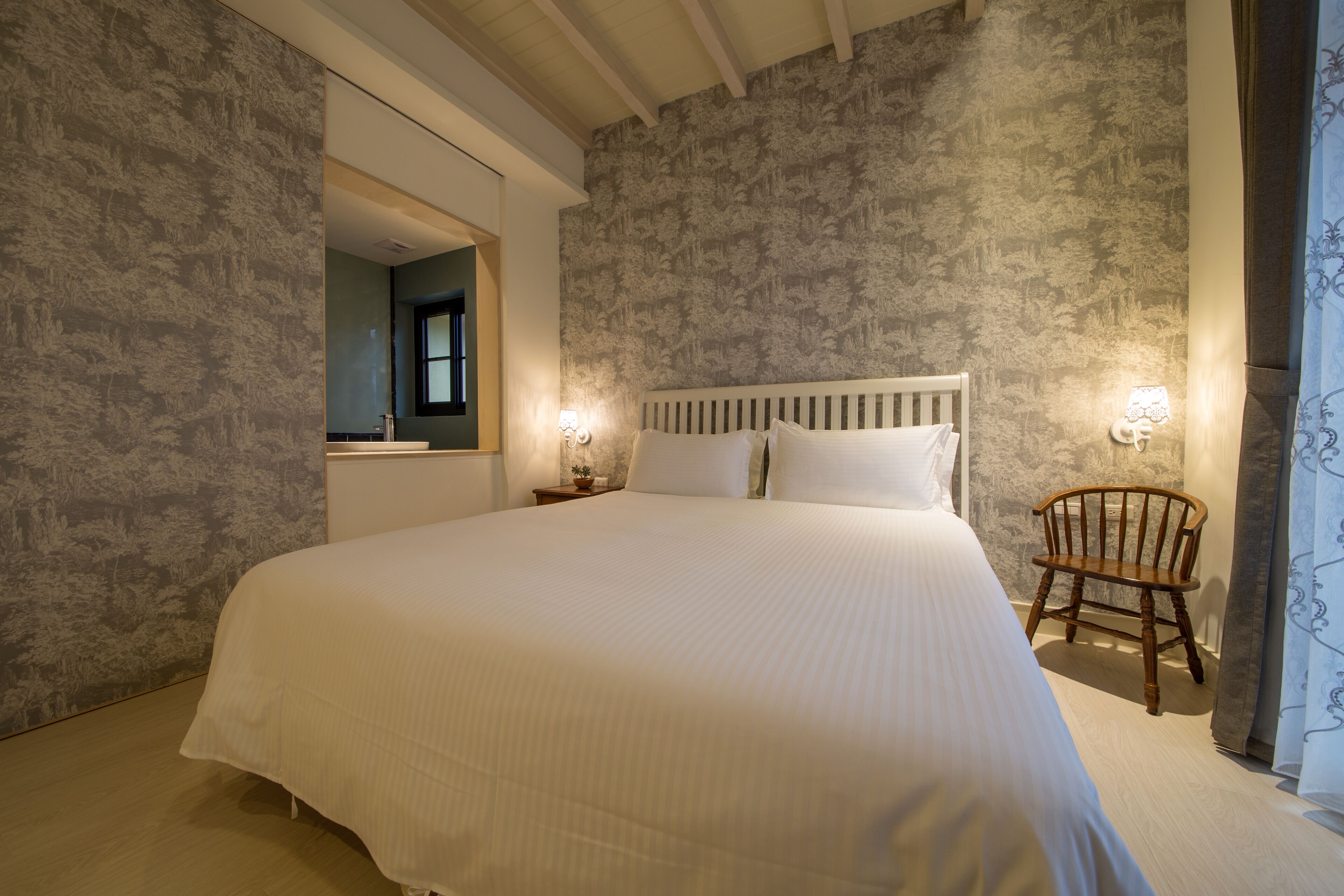 Un dormitorio con una cama grande, una silla de madera y un espejo en la pared.