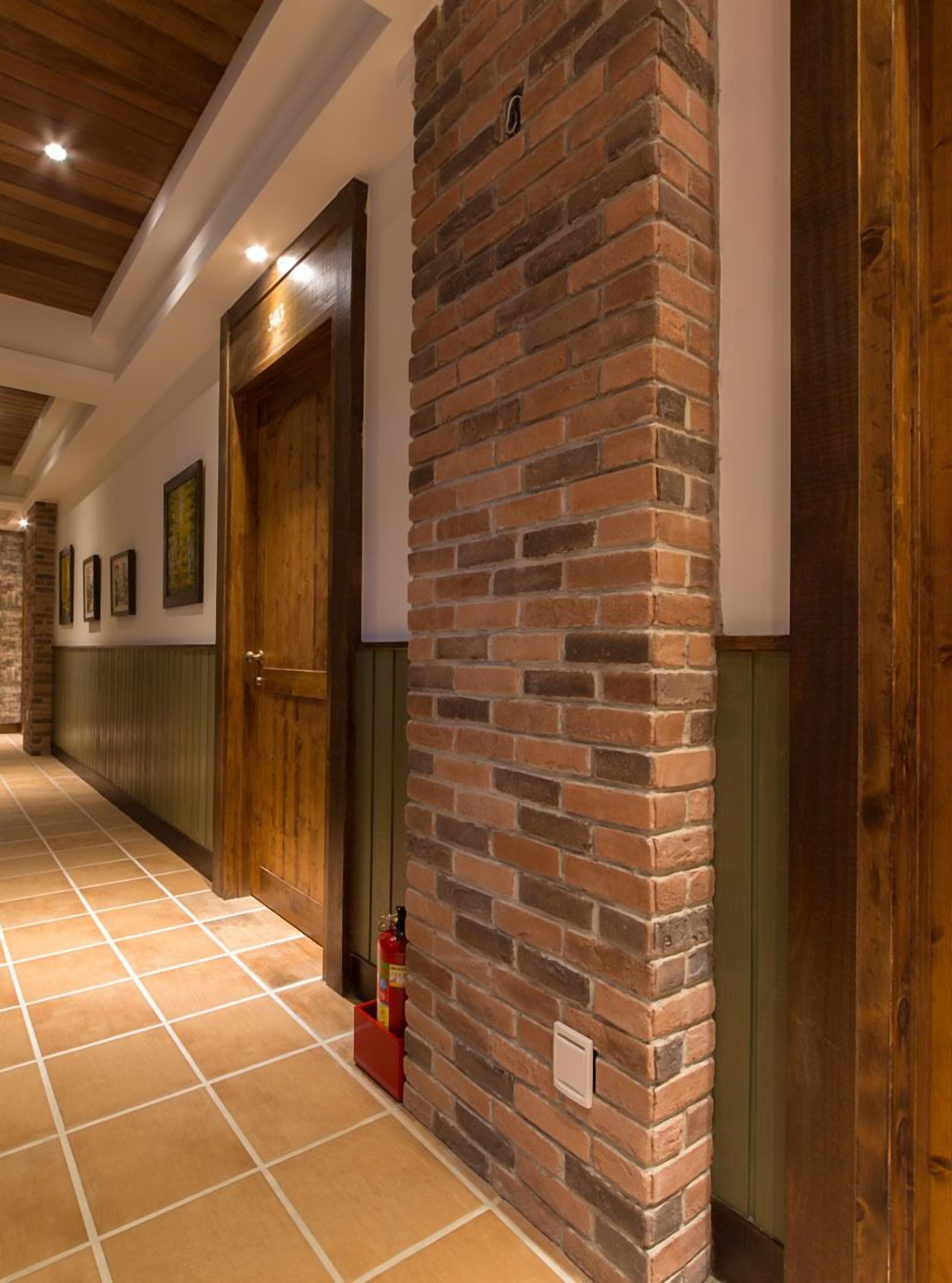 Un couloir avec un mur en briques, des portes en bois et un sol carrelé.