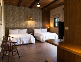 Una habitación con dos camas, techo de madera, pared de piedra, una silla de madera y una mesita.