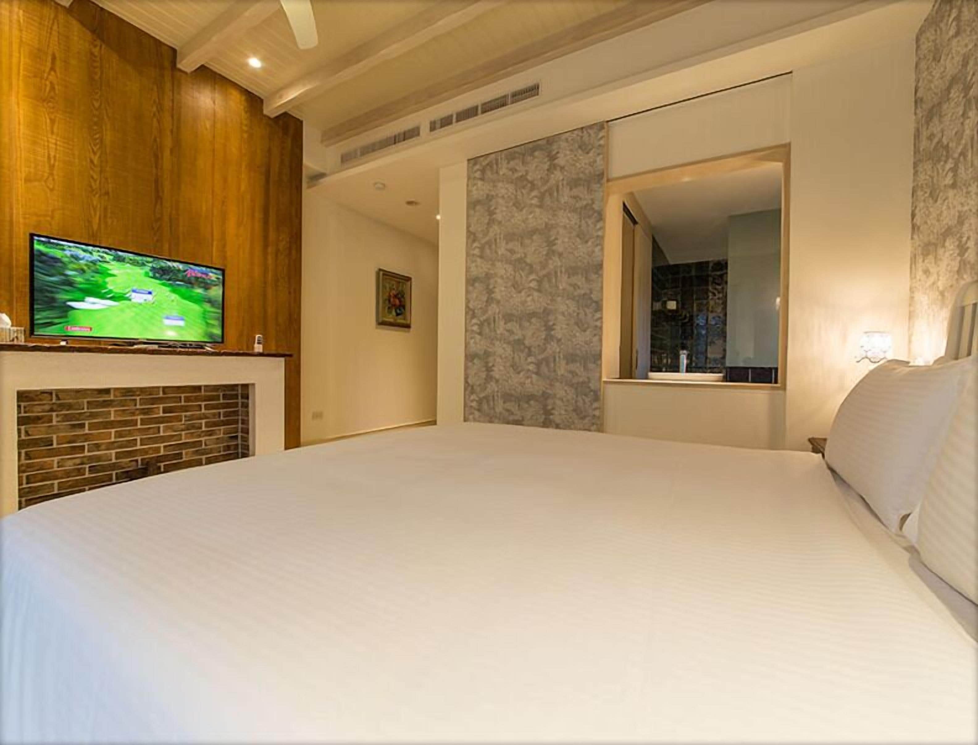 Une chambre d’hôtel avec un grand lit, un téléviseur posé sur une étagère en bois, une cheminée et un miroir au mur.