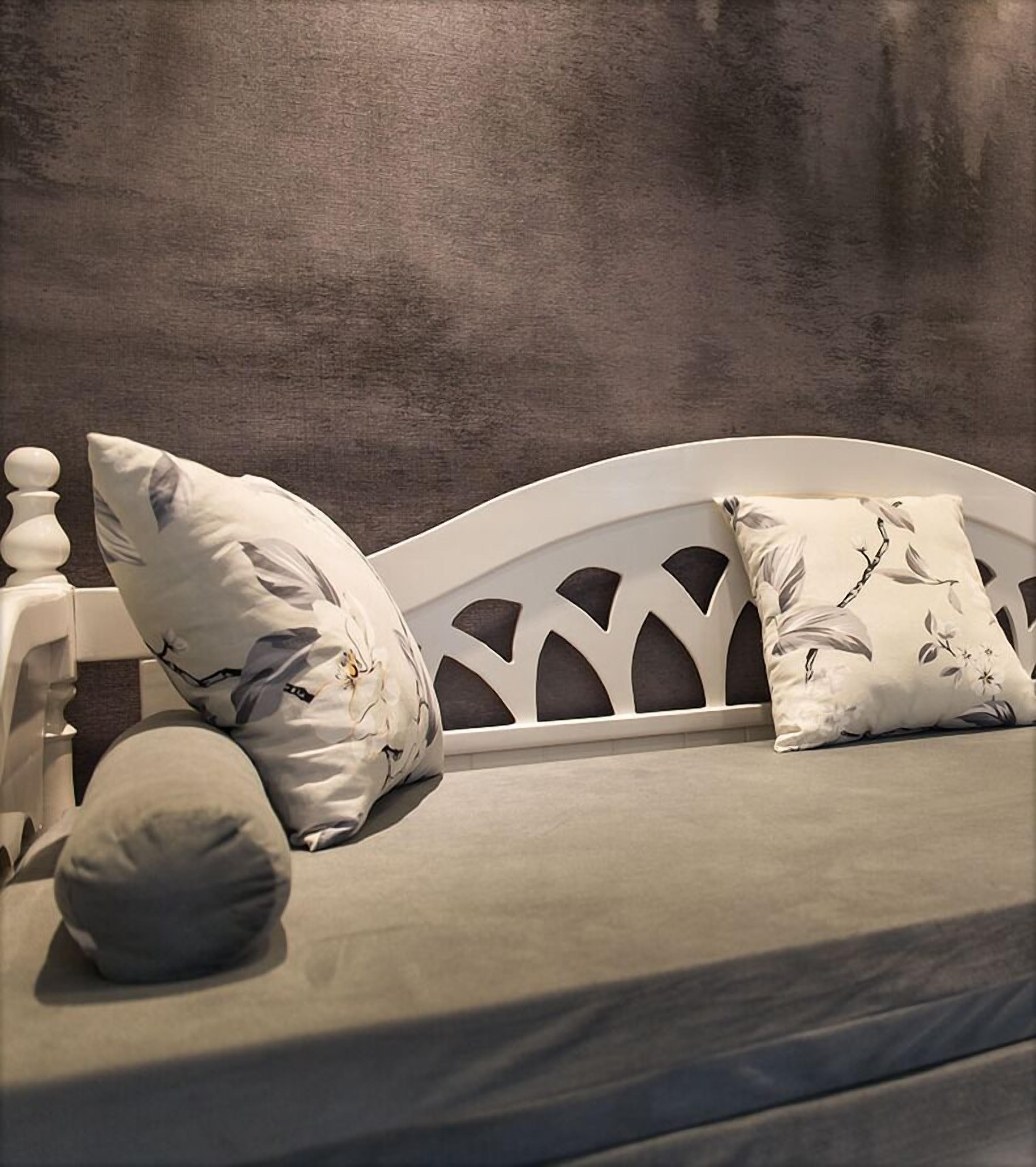 Ein Bett mit weißem Kopfteil, zwei Kissen mit Blumenmuster und einer grauen Decke.