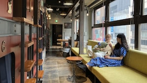 A cozy cafe with wooden shelves, a green sofa, and large windows offering a view of the street. - HARE-TABI SAUNA&INN YOKOHAMA (Yokohama)