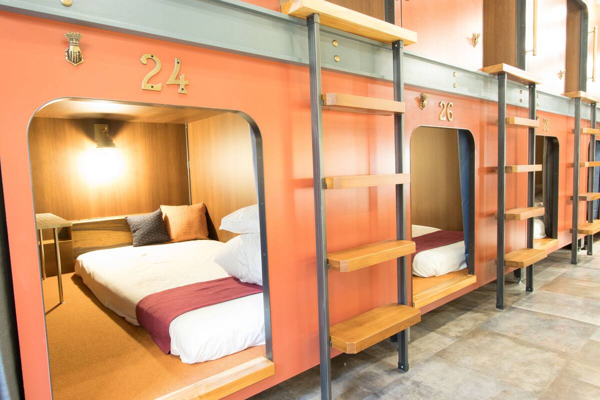 Habitación de hotel con literas, cabecero de madera y el número 24 en la pared.