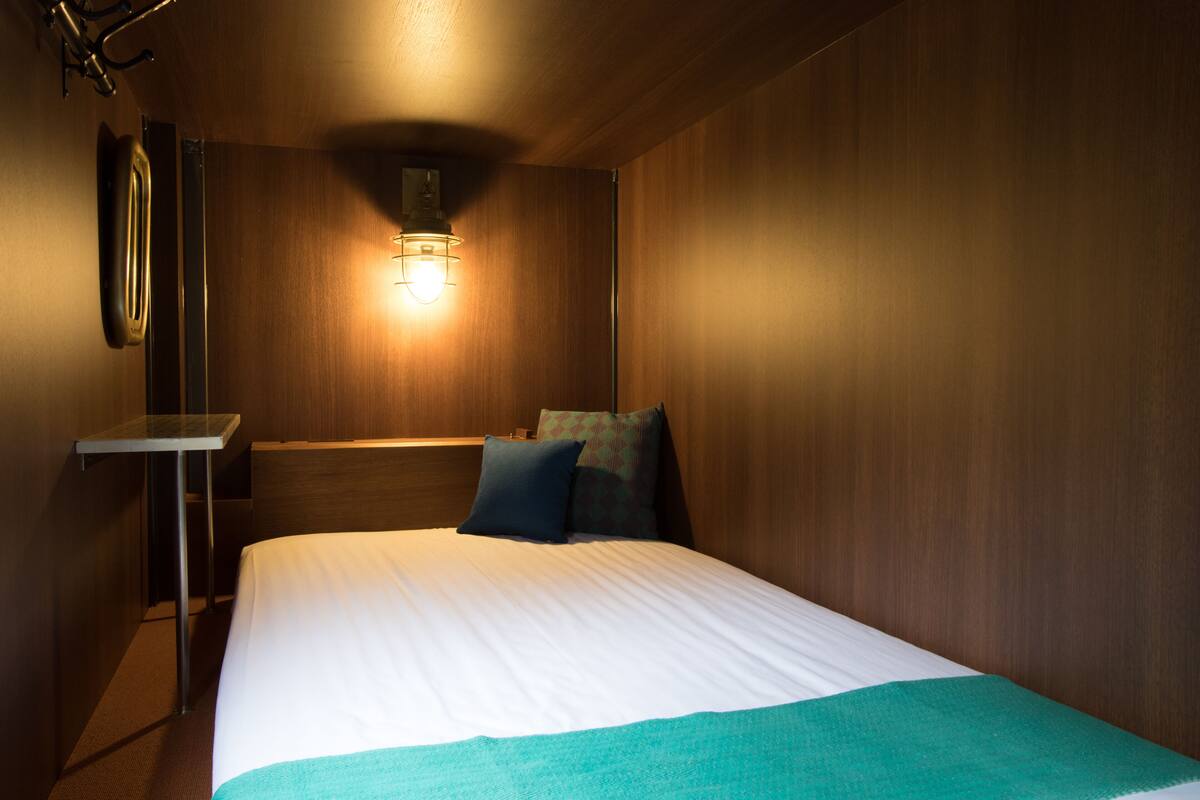 Habitación de hotel con una cama, una mesita de noche, una lámpara de pared y paneles de madera.
