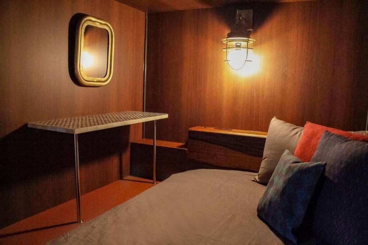 Una habitación pequeña con cama, una mesita, un espejo y una lámpara de pared.