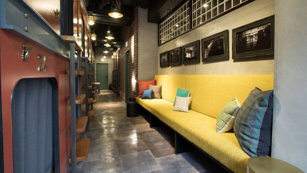 A hallway with a yellow sofa, benches, and a wall with framed pictures. - HARE-TABI SAUNA&INN YOKOHAMA (Yokohama)