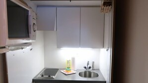 Una kitchenette compacta con microondas, estufa, pileta y un mueble pequeño.