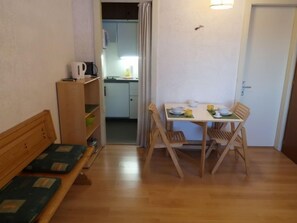 Una habitación pequeña y acogedora con un banco de madera, una mesa de comedor con sillas y una kitchenette al fondo.