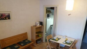 Una habitación pequeña con un banco de madera, una mesa con sillas, un microondas y una estantería con diversos objetos.