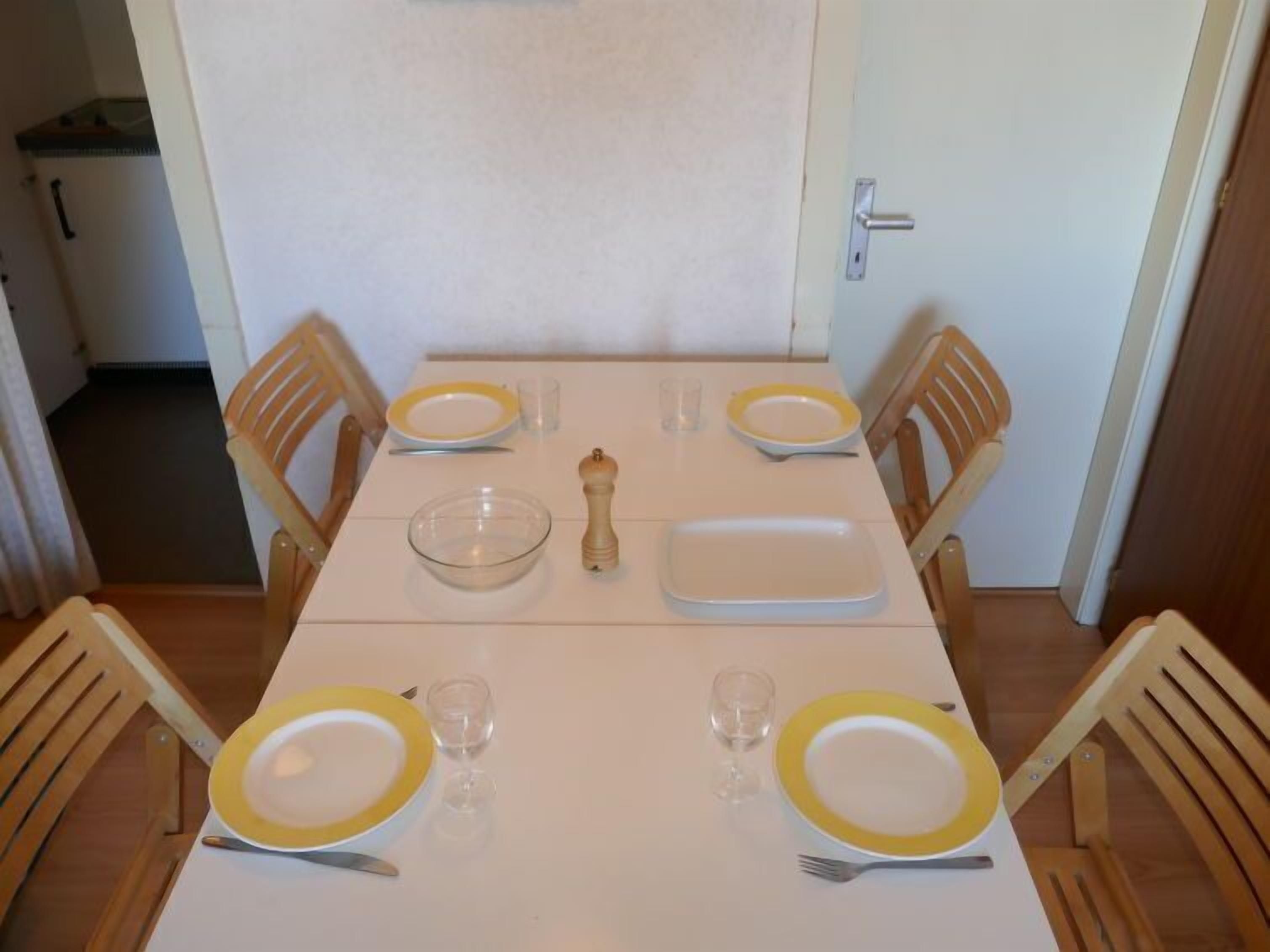 A dining table set with yellow plates, clear glasses, and a salt and pepper shaker.