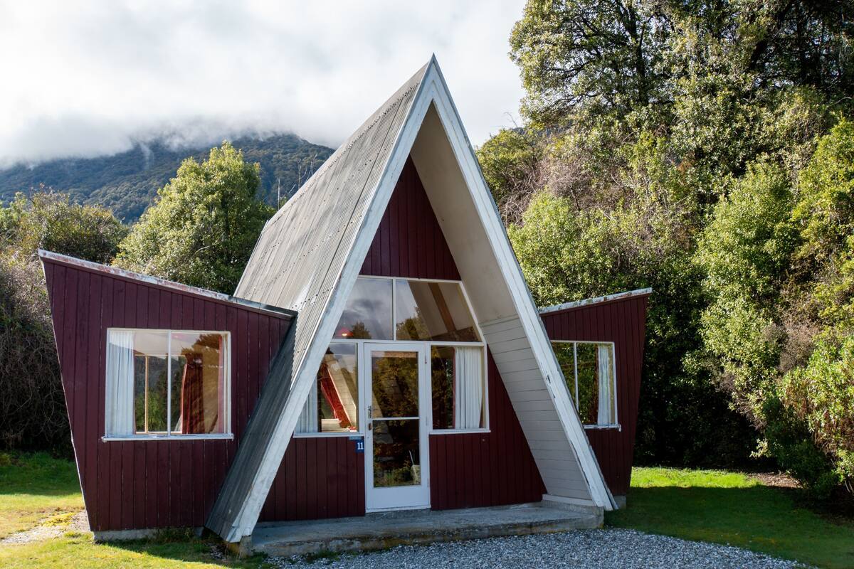 A red, A-frame cabin with a gravel driveway and a grassy area in front.