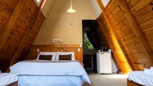 Una camera da letto mansardata accogliente con soffitto in legno, un letto con biancheria bianca, un piccolo frigorifero bianco e un lampadario.