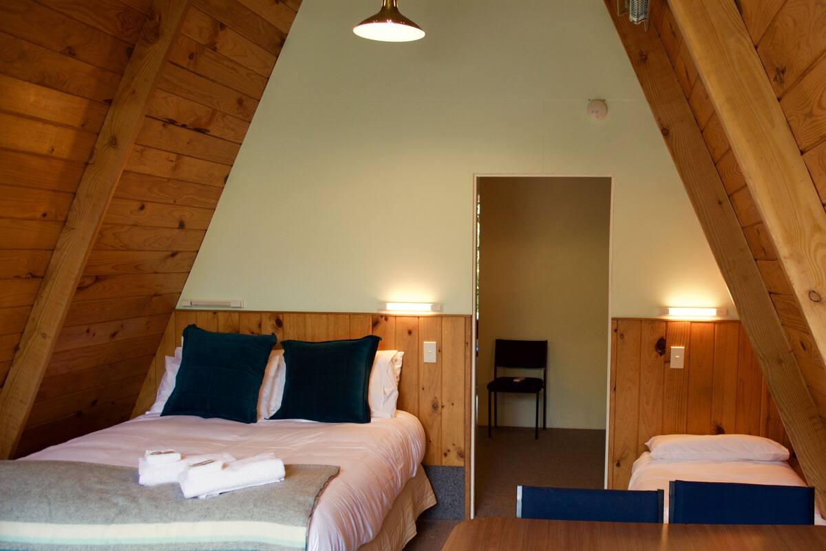 A cozy, triangular room with a bed, a table, and a chair.