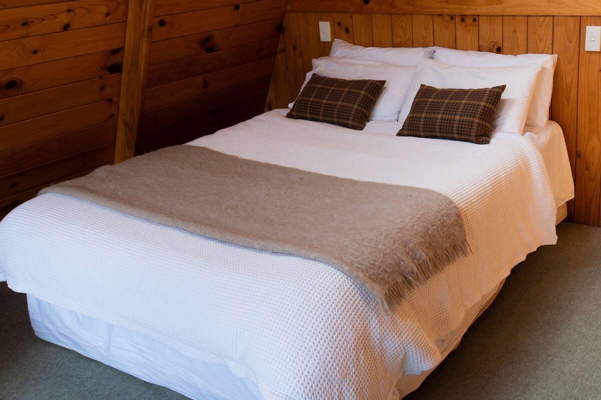 A neatly made bed with a white and beige blanket, two brown pillows, and a wooden headboard.