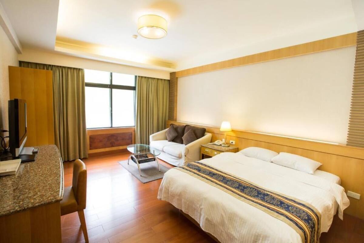 A hotel room with a bed, a desk, a chair, a TV, and a window with curtains.
