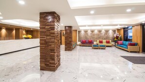 Spaziosa hall con pavimento in marmo, dettagli in legno e diverse zone relax con cuscini colorati.