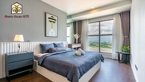 Une chambre moderne avec un grand lit, une table de chevet, une lampe et une vue sur la ville grâce à de grandes fenêtres.