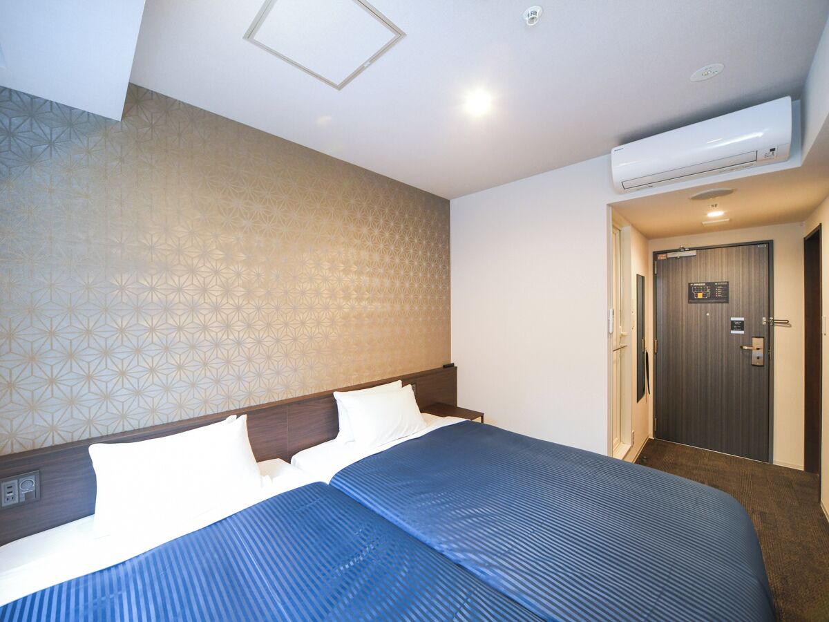 A hotel room with a large bed, a headboard, an air conditioning unit, a door with a sign, and a patterned wall.