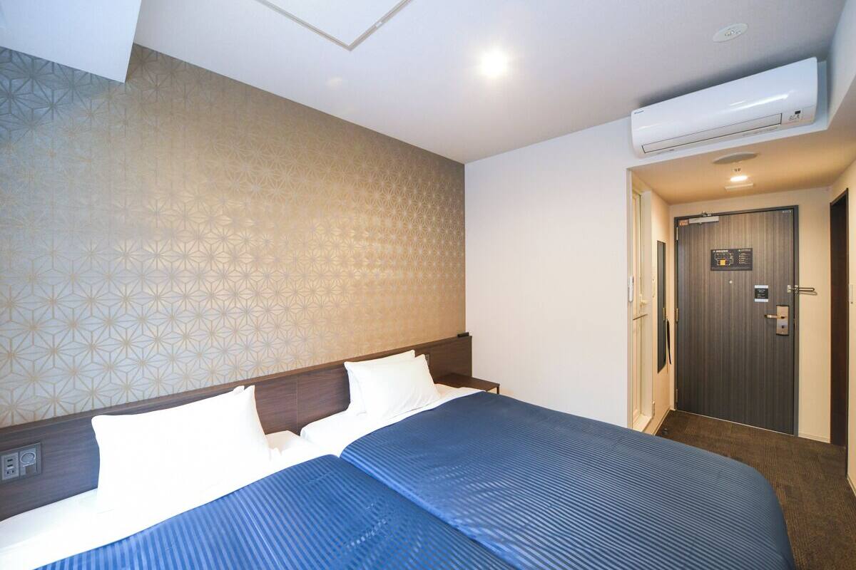 A hotel room with a large bed, a headboard, an air conditioning unit, a door with a sign, and a patterned wall.
