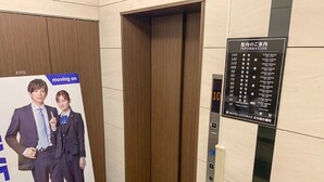 An elevator with a digital display showing the number 10, a sign listing guest room numbers, and a poster with two people and the text "moving on". - HOTEL LiVEMAX Nihonbashi Koamicho (Tokyo)