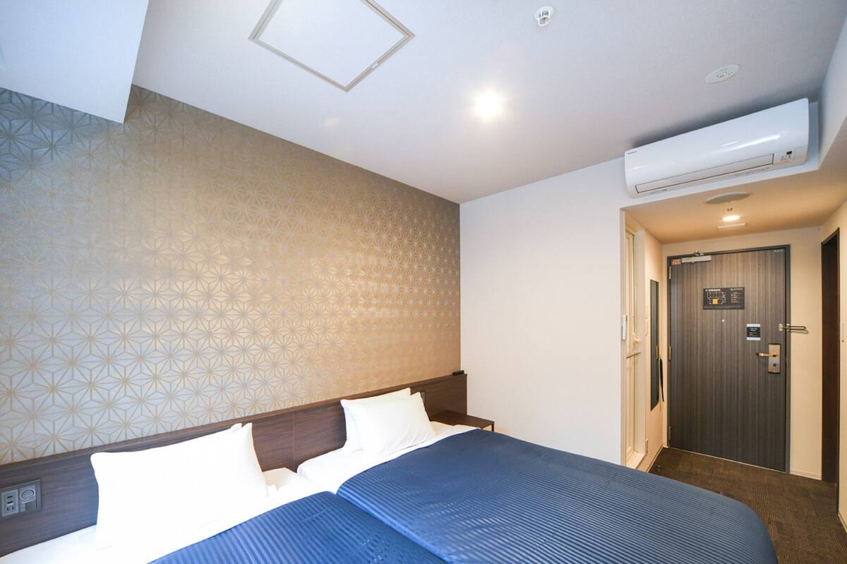 A hotel room with a large bed, a wall-mounted air conditioner, and a door with a sign.