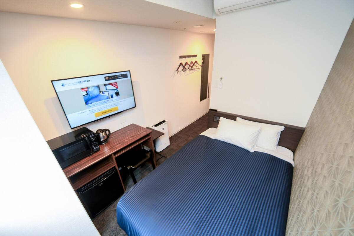 A hotel room with a bed, a desk with a computer, a television, and a small kitchenette.